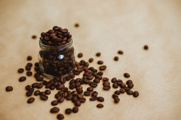 Coffee beans in a glass jar. Dark-colored roasted coffee beans on Kraft paper.