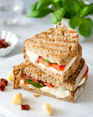 Delicious toast with white asparagus, tomatoes, mozzarella, sun-dried tomatoes and basil on white marble board.