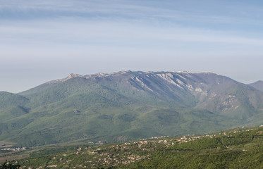 Green mountain range with small peaks, Crimea. Sunrise. Serene picturesque green valley with small village on nearest hill. Scenery of nature of Southern Crimea.