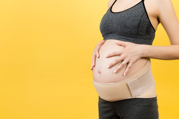 Cropped image of pregnant woman wearing elastic bandage against pain in the back at yellow...