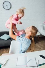 Selective focus of mother holding baby girl near smartphone, calculator and stationery on table