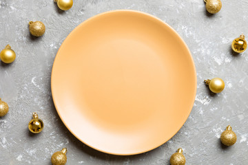 Top view of festive plate with golden baubles on cement background. Christmas decorations and toys. New Year advent concept