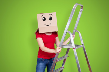 Person with cardboard box on its head and a smiling face standing behind a ladder on fresh green...