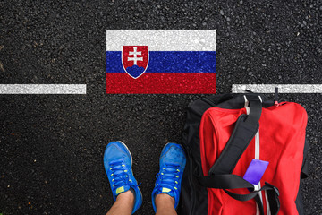 a man with a shoes and travel bag is standing on asphalt next to flag of Slovakia and border 