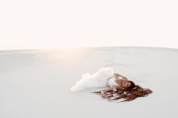 Girl with dreadlocks in a dress in the desert on white sand. Sunset
