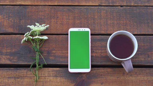 Closeup top view flatlay 4k video footage of modern mobile smartphone with empty blank green screen lying on wooden brown desk background. Woman scrolls green pages of gadget. Banner with copy space.