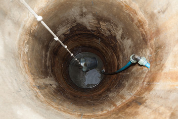 Wnętrze starej studni, zbudowanej z betonowych kręgów z zanurzonym wiadrem na linie. Widok z góry. © AP-STUDIO