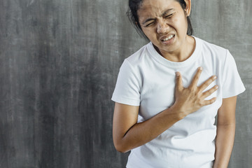 Young Asian woman got chest pain on gray concrete wall for background