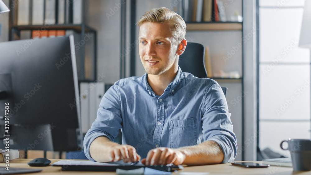 Poster handsome blonde entrepreneur sitting at his desk in the office works on desktop computer, working wi