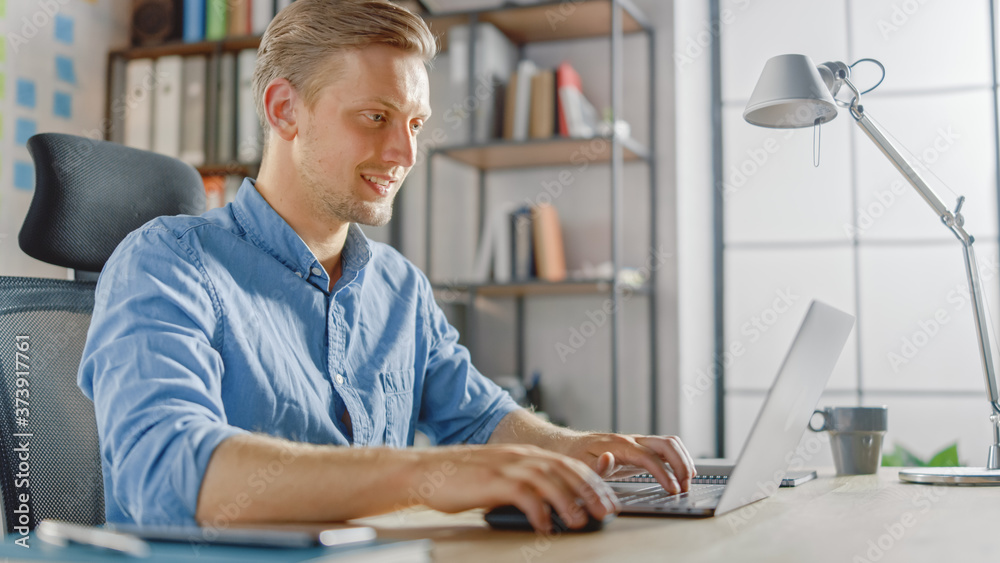 Poster handsome blonde businessman sitting at his desk in the office works on a laptop. creative entreprene