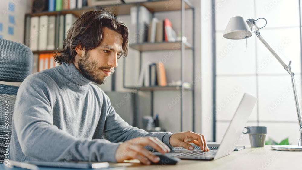 Poster handsome long haired hispanic businessman sitting at his desk in the office works on a laptop. creat