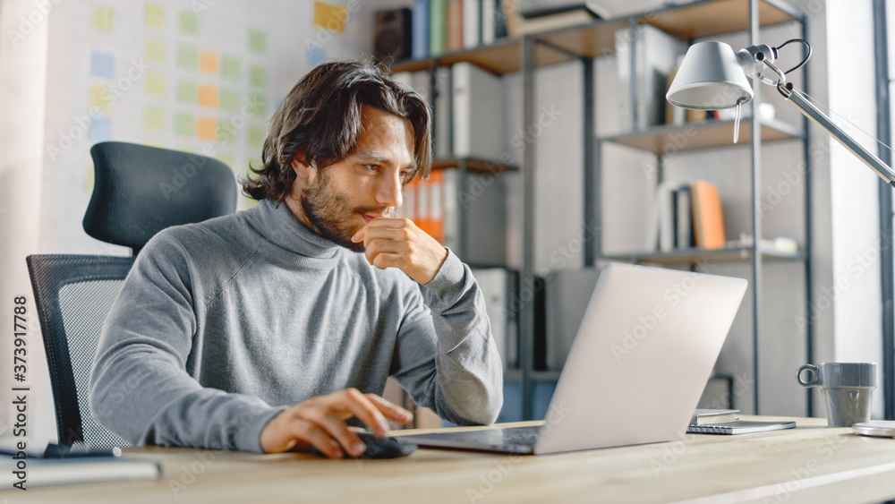 Poster handsome long haired hispanic businessman sitting at his desk in the office works on a laptop. creat