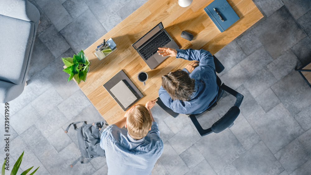 Poster top view shot of a young businessman working at his desk on a laptop, talks with his manager and lis
