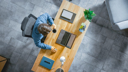 Top View Shot: Businessman Sitting at the Wooden Desk Works on a Laptop in his Home Office. He...