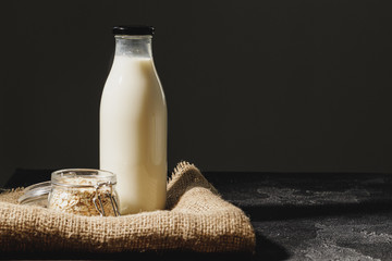 Glass bottle of oat milk with oat flakes in glass jar