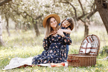 beautiful pregnant woman with little daughter playing on a picnic in a blooming spring garden