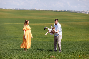 Happy pregnant family with little daughter spending time together in sunny green field on summer day