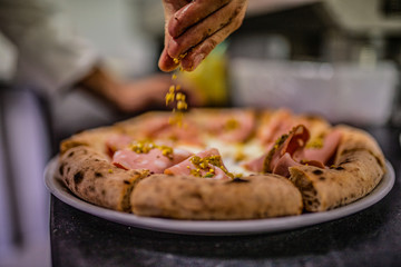 Pizzaiolo mentre mette la granella di pistacchio su una pizza napoletana gourmet