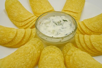 Glass bowl with white sauce stands among potato chips