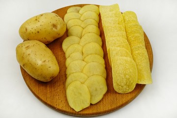 Raw potato tubers, raw potato slices and potato chips lie on a wooden board