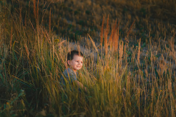 Happy child boy of a resting outdoors on a wild field on sunset. A stylish child with a beautiful smile and dark hair.