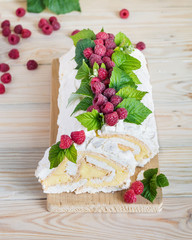 Meringue roll cake with cream and fresh raspberries. Roulade, summer dessert. Selective focus, vertical orientation.