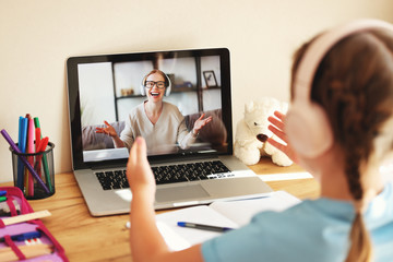 schoolgirl wearing headphones communicates via video link with an online teacher sitting at home