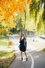 Young trendy woman in autumn city park with coffee in hand. Autumn concept,  woman enjoying  coffee cup on fall day.