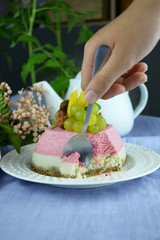 Close-up of hand using a spoon to scoop the raw dessert on white plate. Vegan mini cheesecakes with strawberry and vanilla layer with adding of cashews, cacao butter and coconut milk