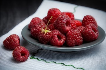 ripe raspberries on a plate on a light linen napkin. Selective focus.