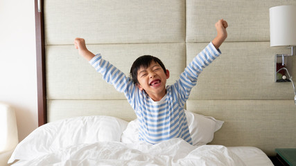 The lovely Asian boy just woke up in the morning and stretched his arms.Happy young kid is on the...