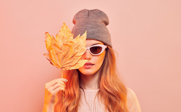 Fashionable hipster woman in Trendy autumn fall outfit, stylish hair, makeup. Redhead model in jumper, fashion jeans having fun smiling. Beautiful girl in autumnal beanie hat with maple leaf