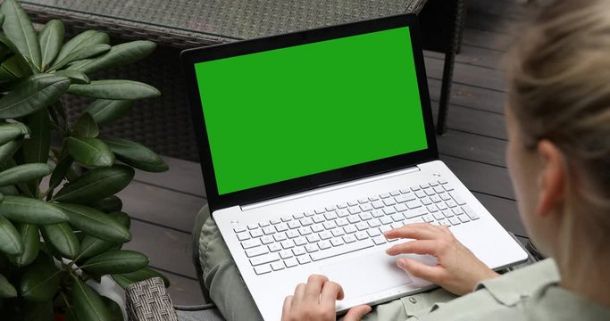 woman using laptop computer on a outdoor terrace, blank green screen mockup copy space