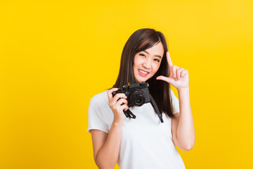 Portrait of happy Asian beautiful young woman photographer holding vintage digital mirrorless photo camera on hands, studio shot isolated on yellow background, lifestyle teenager hobby travel concept