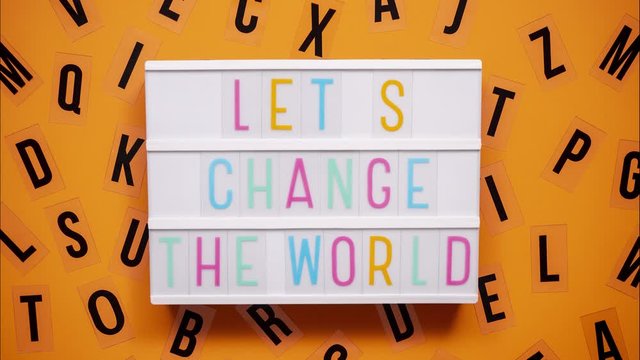 LET'S CHANGE THE WORLD sign on a letter board with letters being animated around. Orange background.