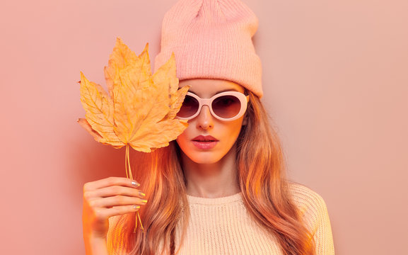 Fashionable hipster woman in Trendy autumn fall outfit, stylish hair, makeup. Blonde model in jumper, fashion jeans having fun smiling. Beautiful girl in autumnal beanie hat with maple leaf