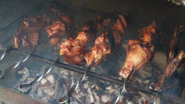 Closeup view of barbeque brazier cooking big turkey or chicken meat leg on metal skewers set flaming on burning coal with fire flame and smoke. traditional east european bbq party home backyard food