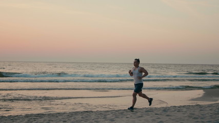 Athletic Man is Jogging on Beach and Running along Sea Coast at Sunset