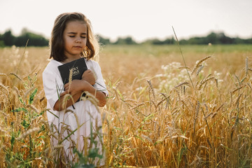 Girl holds bible in her hands. Reading the Holy Bible in a field. Concept for faith, spirituality...