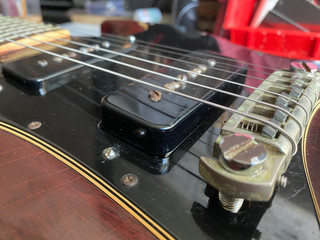 Close up photo An old black guitar pickup with a solid magnet. As if used for a long time Mounted on a cherry-colored electric guitar. use for music store, repair shop.. © warin