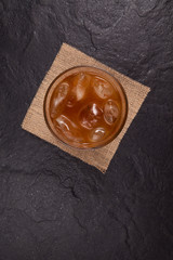Iced coffee with ice in a transparent glass on a dark stone surface, top view