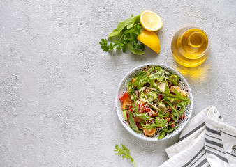 Fresh salad mixed with arugula, tomatoes, cucumbers and grated cheese  on concrete background top view. Healthy food.