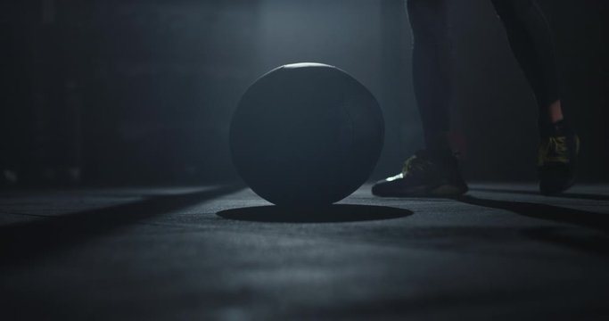 Perfect muscle body guy in a dark cross fit class using a ball to start his training workout