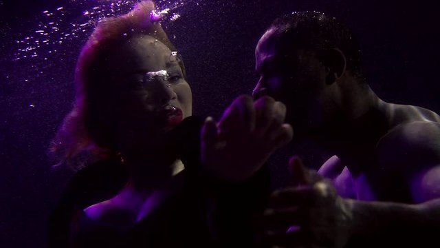beautiful woman with red lips and her black boyfriend are floating underwater in darkness