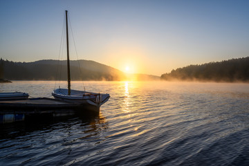 Fototapeta na wymiar Beautiful sunrise view of mountain lake with wooden bridge and boats