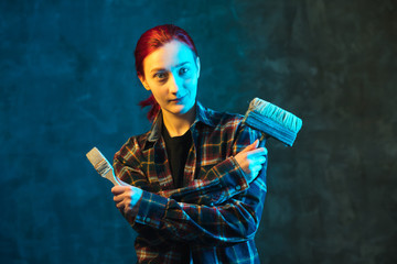 Young woman worker in plaid shirt with colorful neon light. Girl painter holds brush in her hand. Female mastery concept.