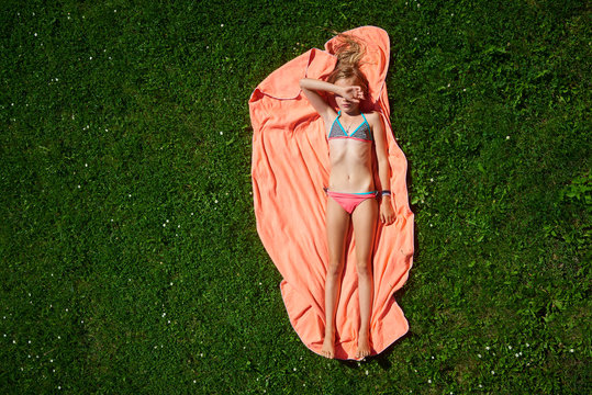 Child girl lying on a towel on a green lawn and sunbathing on a hot summer day. Children summer activities. Copy space