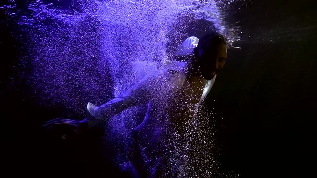 man is sinking in dark water, view from depth, moving hands and swimming