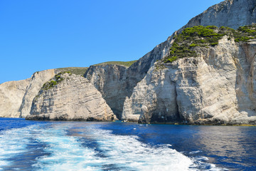 Fototapeta na wymiar Gray rocks on the blue waters of the Mediterranean Sea in Greece. Motorboat traces on the water