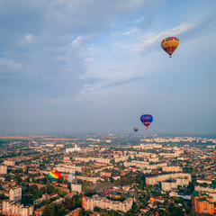 Colorful hot air balloons flying over small european city at summer sunset